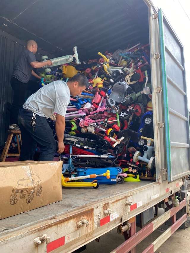Workers loading children's toys and scooters into a shipping container